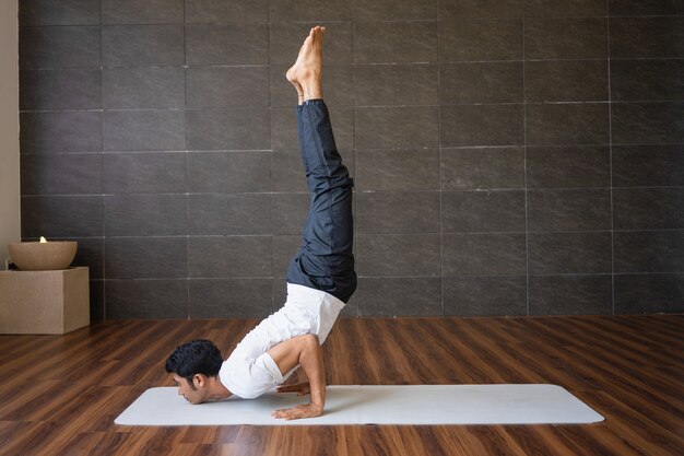 Yogui experimentada que hace posición de la yoga de la parada de manos en gimnasio