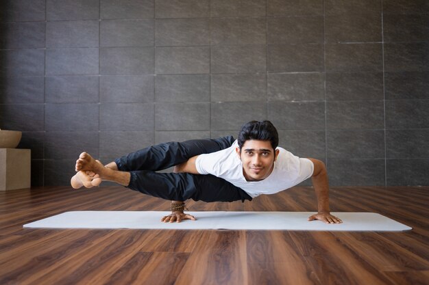 Yogui sonriente que hace actitud lateral de la yoga de la grúa en gimnasio