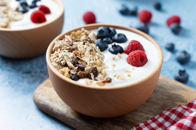 Yogur con bayas y muesli para el desayuno en un tazón sobre fondo azul.