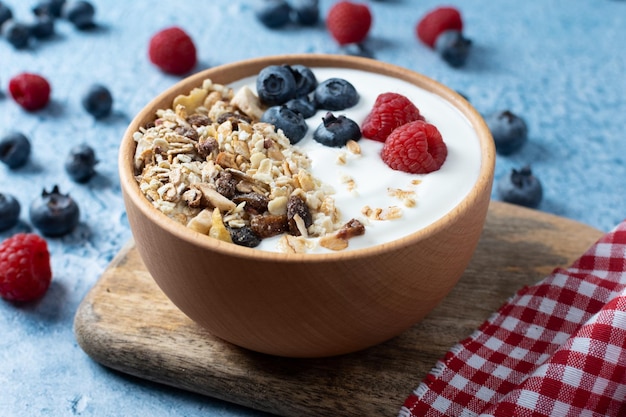 Yogur con bayas y muesli para el desayuno en un tazón sobre fondo azul.