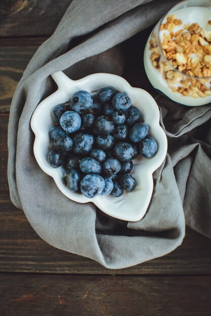 Yogur con granola y arándanos frescos en recipiente de vidrio sobre fondo de madera vieja Efecto vintage