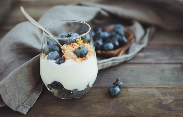 Yogur con granola y arándanos frescos en recipiente de vidrio sobre fondo de madera vieja Efecto vintage