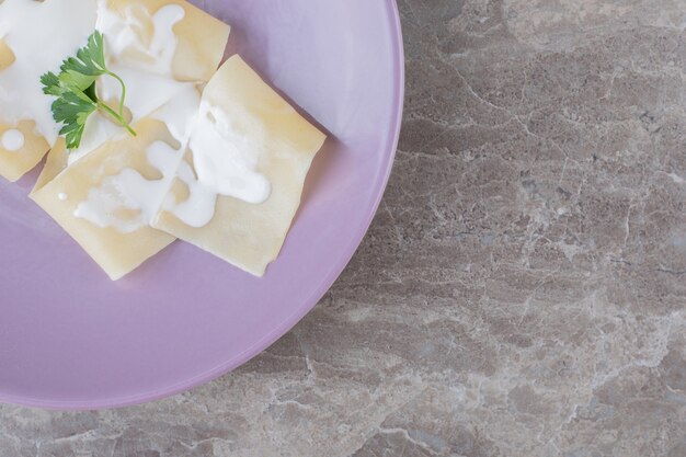 Yogur en láminas de lasaña con verduras en el plato, sobre el mármol.