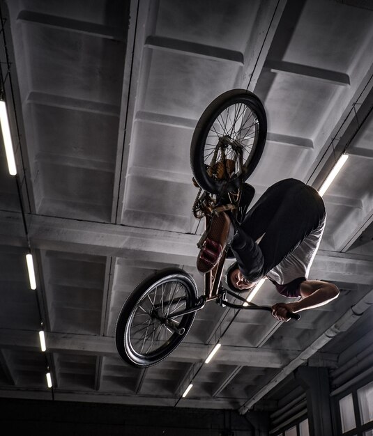 Young BMX haciendo trucos locos en su bicicleta en skatepark en el interior. BMX estilo libre.