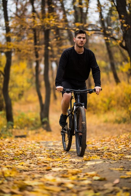 Young fit hombre durante un paseo en bicicleta en un día soleado en el parque otoño