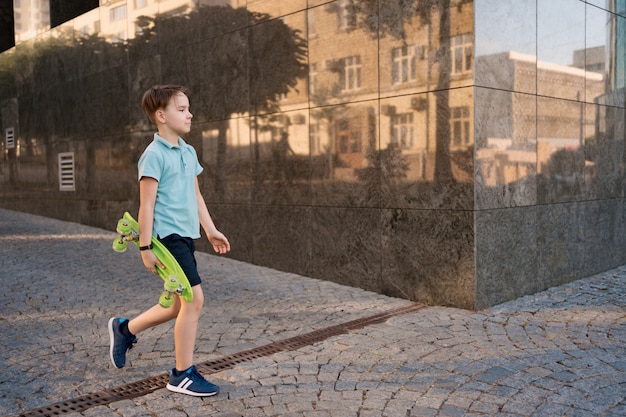 Foto gratuita young school cool boy con ropa brillante caminando con penny board en las manos