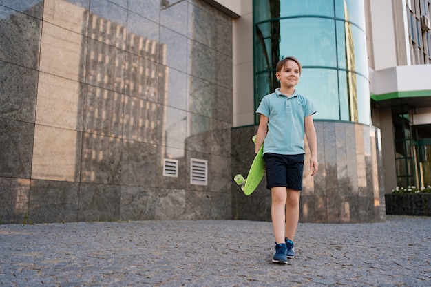 Young SCHOOL cool BOY con ropa brillante caminando con PENNY BOARD en las manos