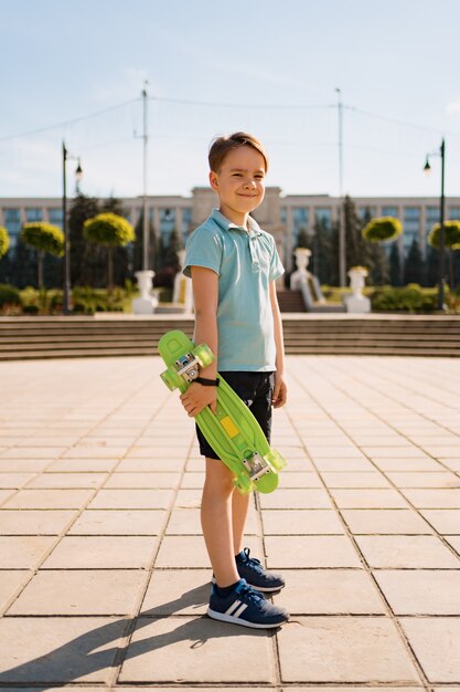 Young SCHOOL cool BOY en ropa brillante de pie con PENNY BOARD en las manos