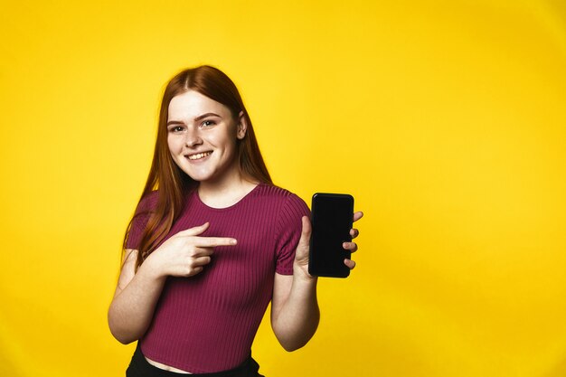 Young sonrió pelirroja caucásica está sosteniendo un teléfono inteligente