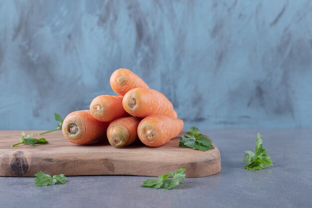 Zanahorias crudas con verduras en la tabla de cortar, en la superficie de mármol.