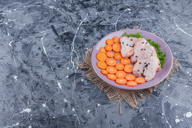 Zanahorias en rodajas, alas y verduras en un plato sobre una arpillera, en el azul.