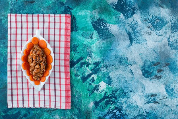 Zanahorias en rodajas y frijoles en un plato sobre el paño de cocina, sobre el fondo azul.