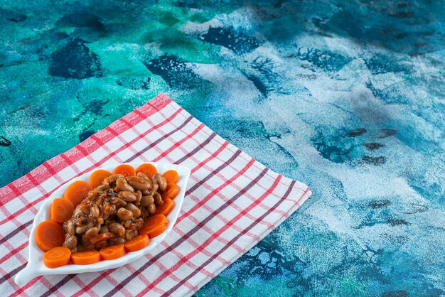 Zanahorias en rodajas y frijoles en un plato sobre el paño de cocina, sobre la mesa azul.