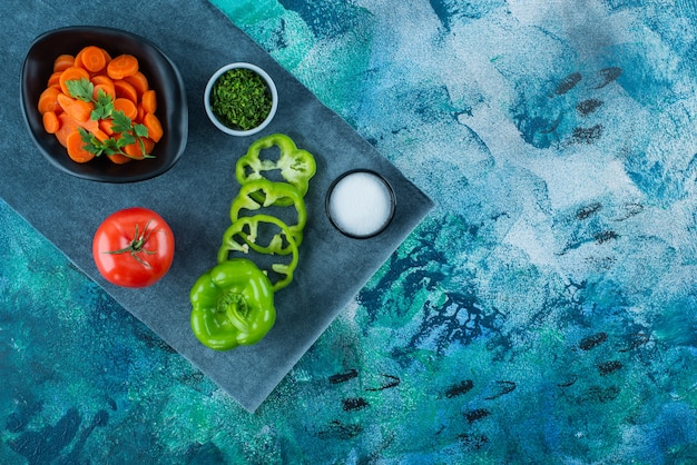 Zanahorias en rodajas en un recipiente junto a las verduras sobre una toalla, sobre el fondo azul.