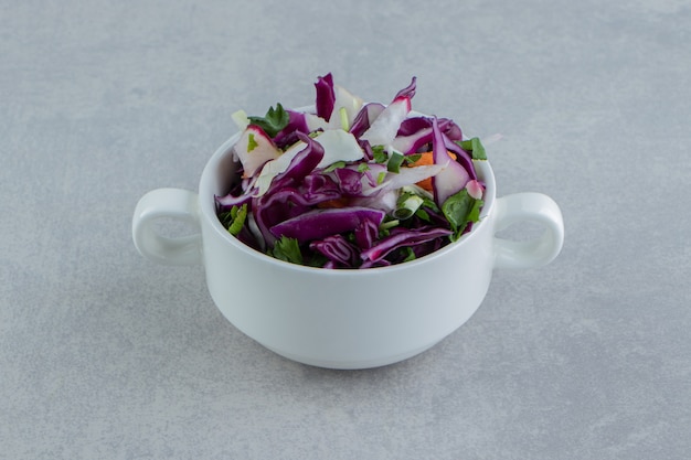 Zanahorias en rodajas, repollo, verduras, en una taza, sobre el fondo de mármol.