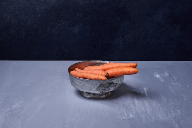 Zanahorias en una taza metálica sobre mesa azul.