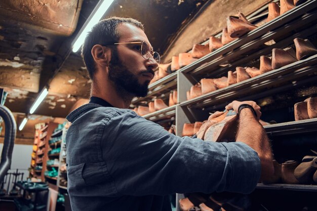 Zapatero barbudo enfocado está buscando la forma correcta del zapato en el almacenamiento.