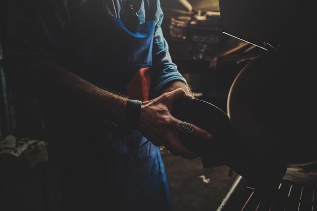 Zapatero en delantal está trabajando en zapatos usando una máquina especial en su taller.