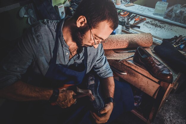 Zapatero diligente está trabajando en suela de zapato usando un martillo en su oscuro lugar de trabajo.