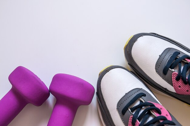 Zapatillas de deporte y mancuernas fitness sobre un fondo blanco. Diferentes herramientas para el deporte. Concepto estilo de vida saludable, el deporte y la dieta. Equipo de deporte. Copie el espacio. Accesorios planos de fitness y entrenamiento