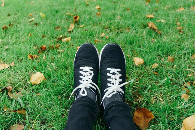 Zapatillas de juventud en las piernas de la muchacha en la hierba durante el día soleado de verano sereno.