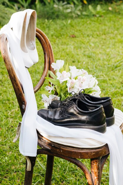 Zapatos de boda negros y tacones blancos con un ramo de flores en una silla de madera en el jardín