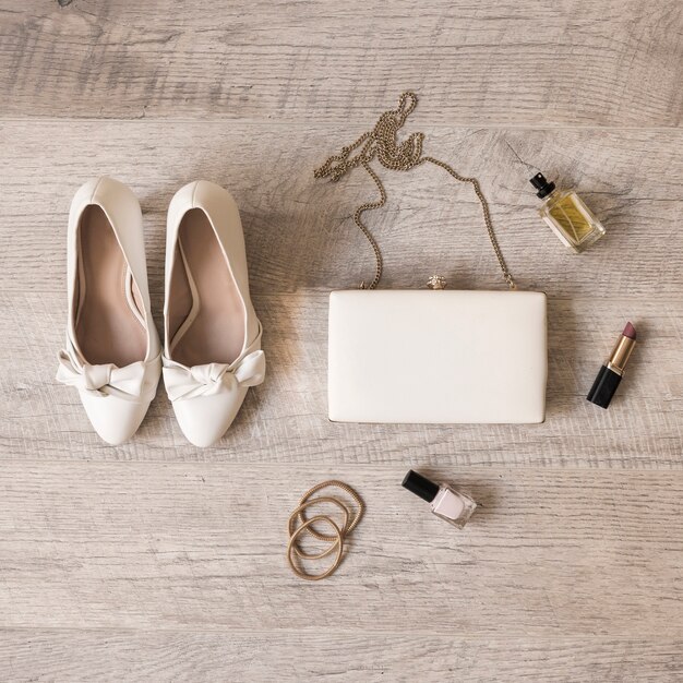 Zapatos de novia blancos; perfume; lápiz labial; cintas para el pelo; Clutch y cintas para el pelo sobre fondo de madera.