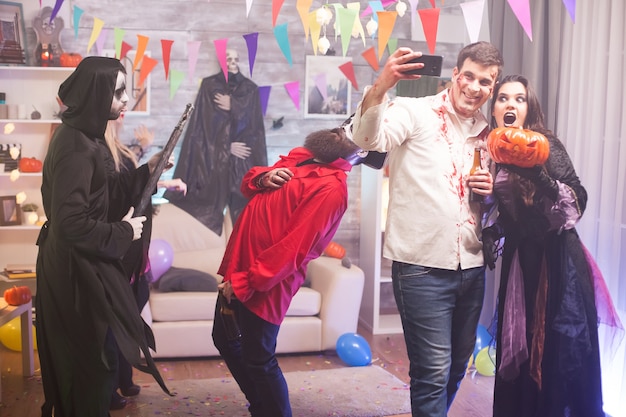 Zombie masculino tomando un selfie con mujer bruja sosteniendo una calabaza en la celebración de halloween.