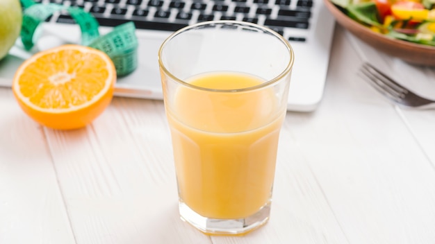 Un zumo de naranja y una computadora portátil en el escritorio de madera blanca