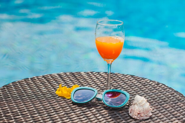 Zumo de naranja y gafas de sol con piscina de fondo