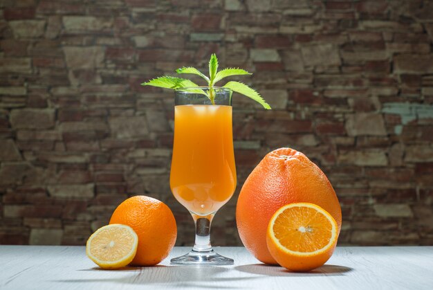 Zumo de naranja con menta, cítricos en una copa sobre fondo de madera y piedra de ladrillo, vista lateral.