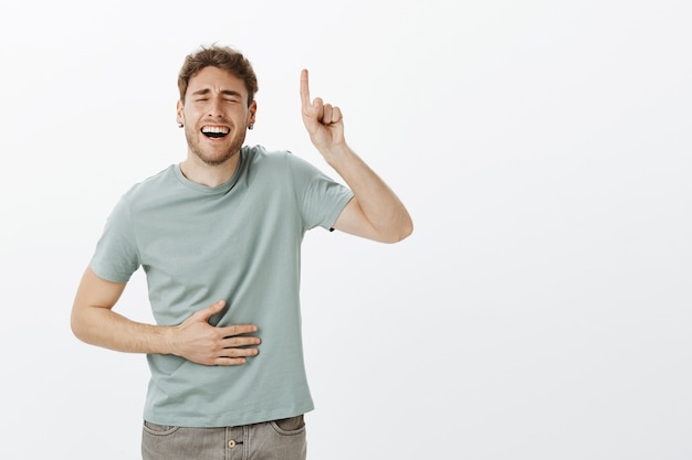 A Guy piace la donna con senso dell'umorismo. Ritratto di modello maschio divertente bello in maglietta casual, ridendo ad alta voce con gli occhi chiusi e un ampio sorriso