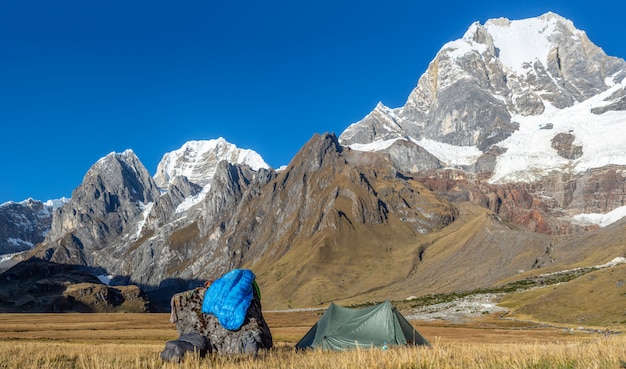 Abbellisca il colpo di una tenda verde vicino ad una roccia in un campo circondato dalle montagne coperte di neve