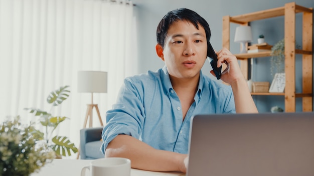 Abbigliamento casual freelance Asia guy utilizzando laptop parlare sul telefono cellulare in salotto a casa.