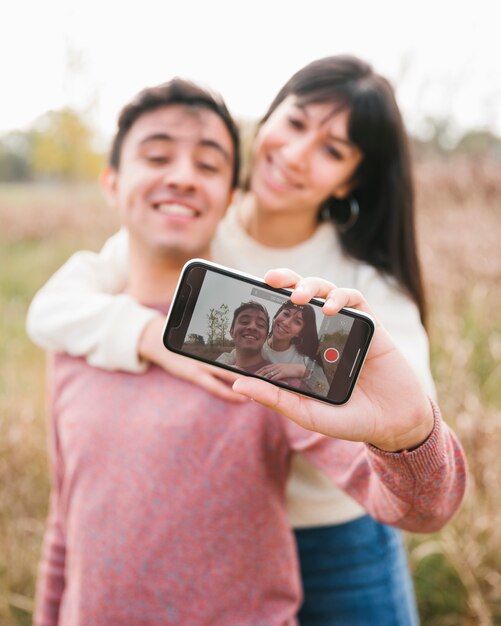 Abbracciando le giovani coppie che prendono i selfie con lo smartphone