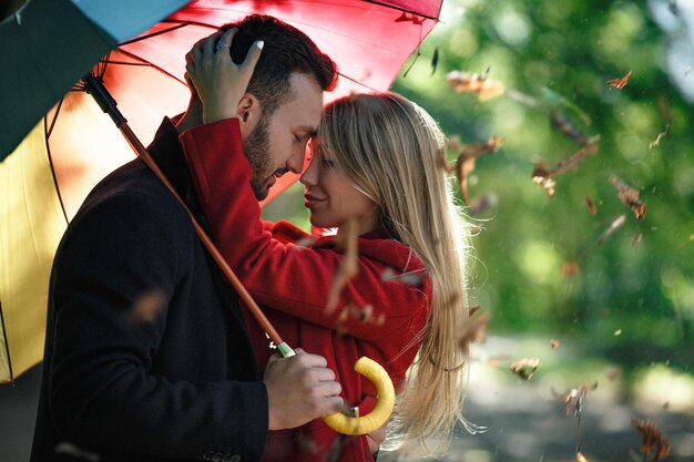 Abbracciare la coppia di innamorati sotto l'ombrello colorato nel parco. Trascorrere del tempo insieme. Concetto di amore.
