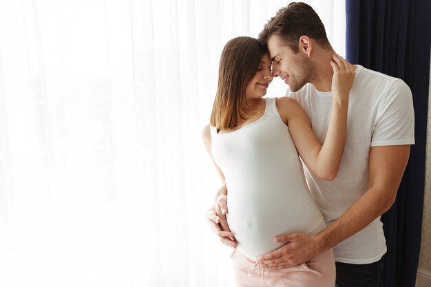 Abbraccio felice dell'uomo sua moglie incinta adorabile all'interno a casa