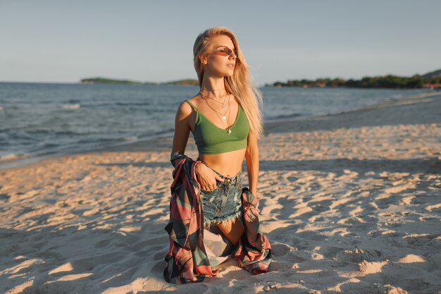 Abbronzatura sottile donna con lunghi capelli biondi in posa sulla spiaggia tropicale.