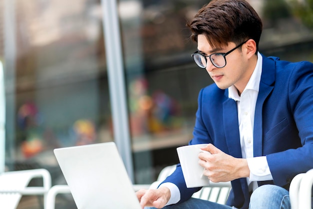 Abito formale uomo d'affari intelligente sedersi rilassarsi tenere in mano smartphone con computer portatile di lavoro televideo conferenza riunione lavoro a distanza sociale distanzaasian ale lavoro rilassarsi in giardino parco sfondo