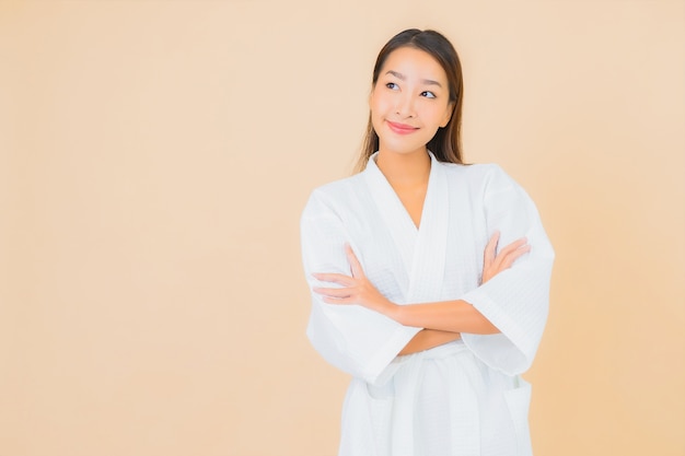 Accappatoio da portare della bella giovane donna asiatica del ritratto con il sorriso sul beige