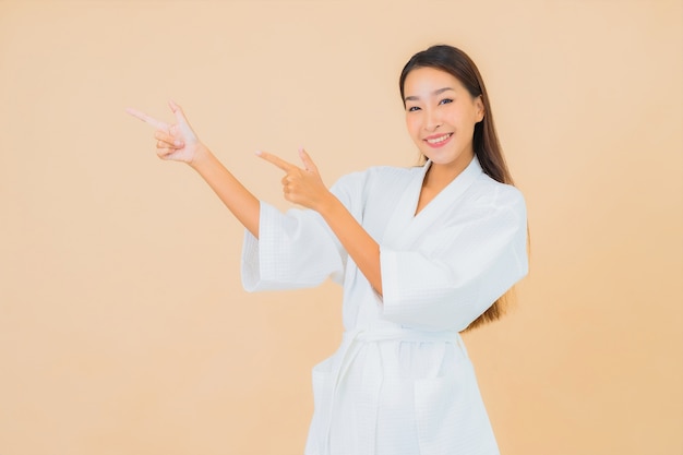 Accappatoio da portare della bella giovane donna asiatica del ritratto con il sorriso sul beige