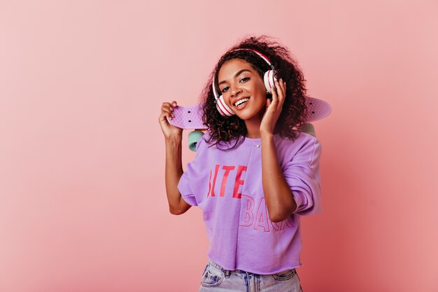 Accattivante ragazza nera spensierata ascoltando musica. Studio shot di jocund modello femminile africano in posa in cuffie.