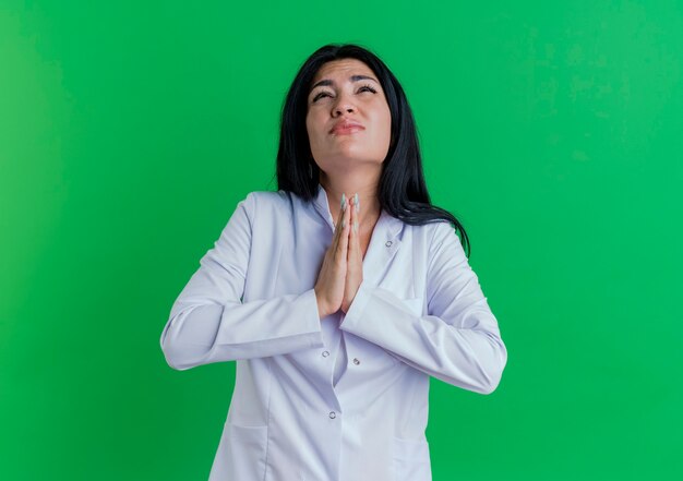 Accattonaggio giovane medico femminile che indossa abito medico cercando di tenere le mani unite nel gesto di pregare