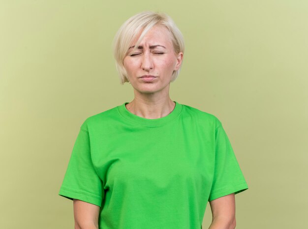 Accigliata donna bionda di mezza età slava in piedi con gli occhi chiusi isolati su sfondo verde oliva