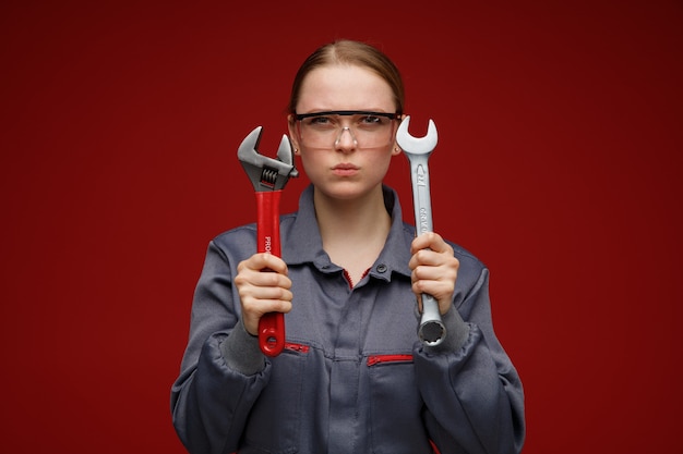 Accigliato giovane ingegnere femmina bionda che indossa occhiali di sicurezza e uniformi che tengono le chiavi
