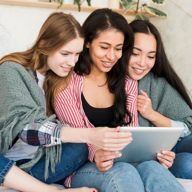 Accoccolandosi sotto le ragazze coperte che si siedono e guardando lo schermo del tablet