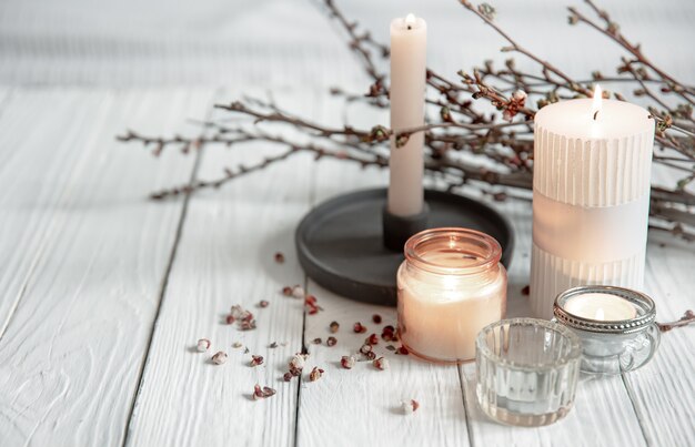 Accogliente composizione con candele fiammeggianti e giovani rami di alberi su una superficie di legno in stile scandinavo.
