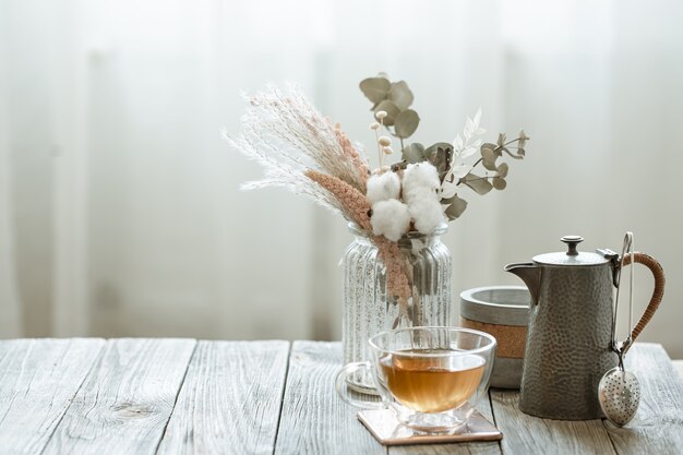 Accogliente natura morta con tazza di tè in vetro, candele ed elemento a maglia su sfondo sfocato spazio copia.