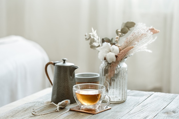 Accogliente natura morta con tazza di tè in vetro, candele ed elemento a maglia su sfondo sfocato spazio copia.
