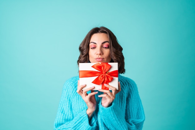 Accogliente ritratto di una giovane donna con un maglione blu lavorato a maglia e un trucco rosa brillante con in mano una scatola regalo